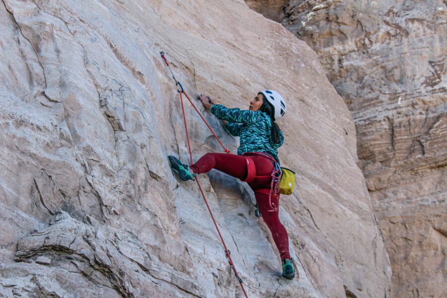 Tripod Position | Send Edition A female climber wearing a white helmet and red pants demonstrating the tripod position by using three points of contact on a granite wall.